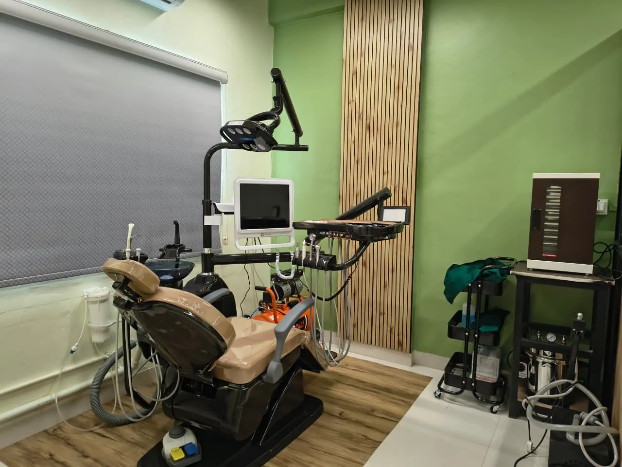 Dental chair, delivery unit and sterilisation equipment against a green wall with timber slats