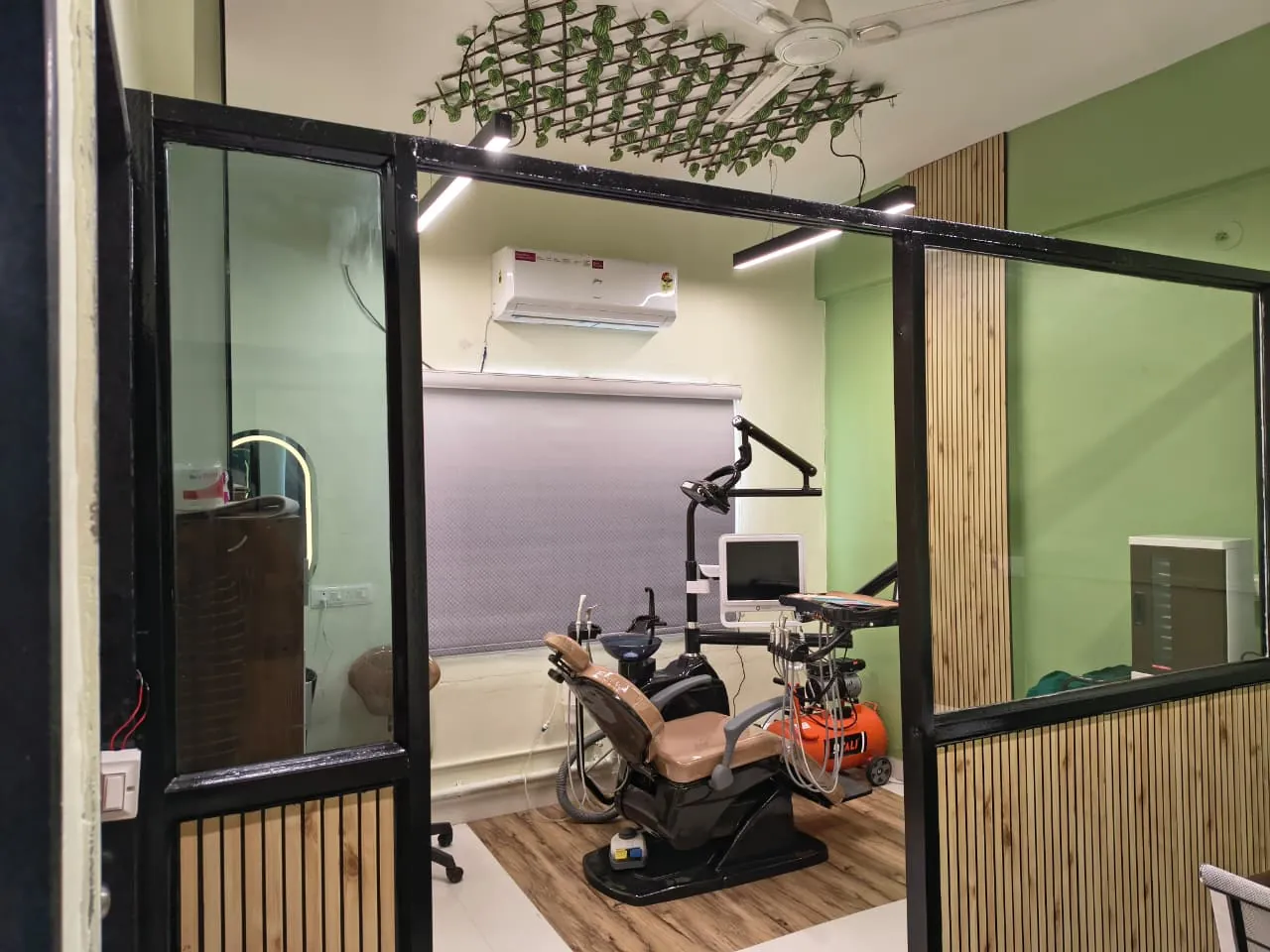 Glass and black-steel partition into the treatment room, greenery trellis on the ceiling